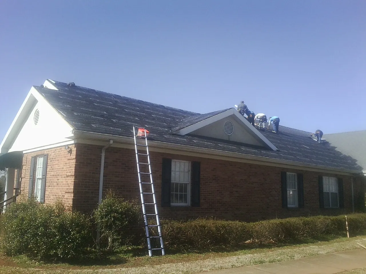 Crew tearing shingles off a brick ranch roof with a ladder set — Emergency Roof Repair work by our crew in Eutawville