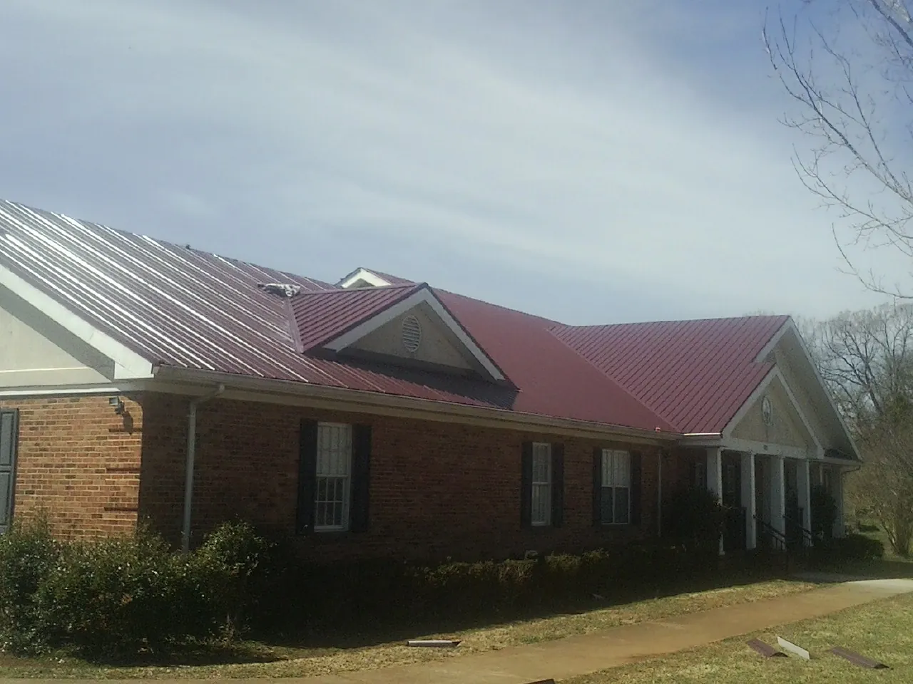 Red metal roof with gabled entries on a long brick building, from a Hail Damage Roof Repair job in Eutawville