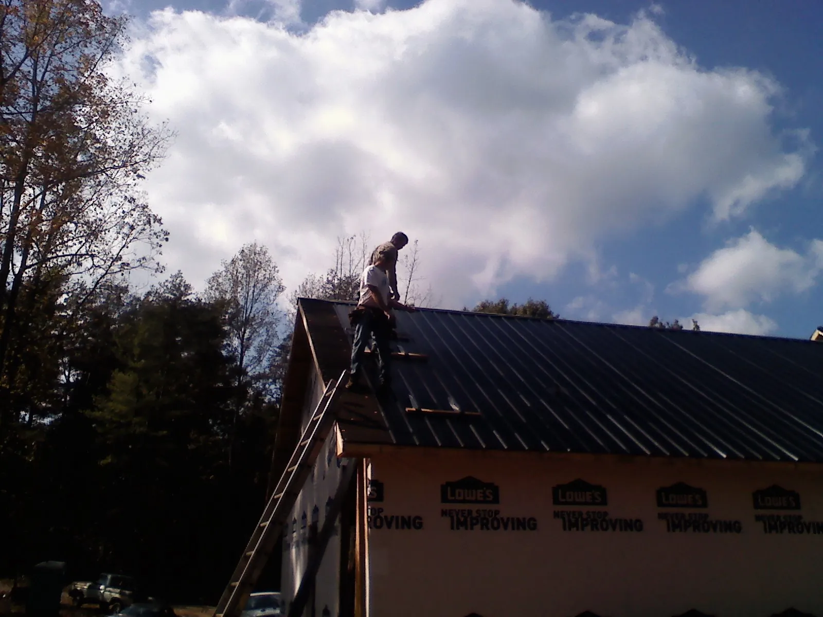 Roofer fastening dark metal panels high against a cloudy sky, from a Roof Inspection job in Eutawville