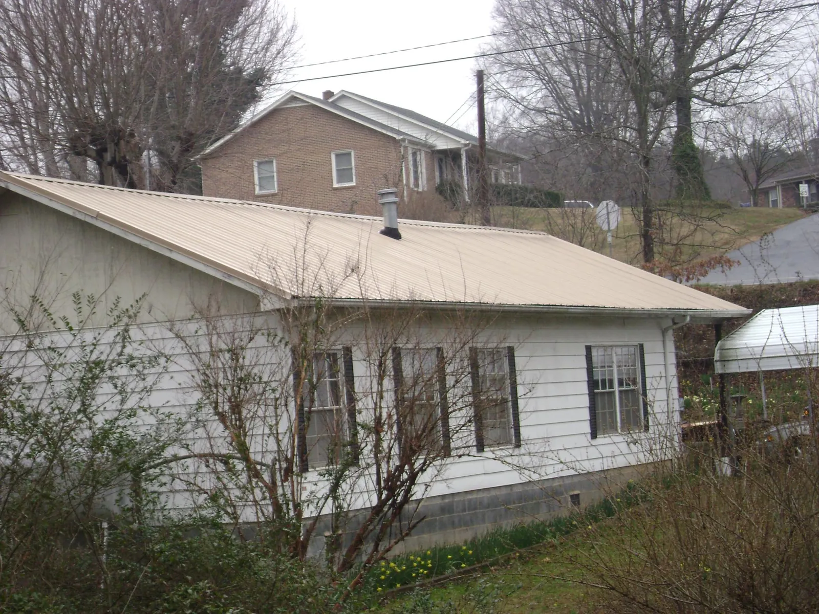 Tan metal roof on a white sided house set into a hillside — Commercial Roofing by Roofing Brothers in Eutawville